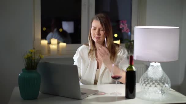 Mujer joven que trabaja en el ordenador portátil en la oficina en casa por la noche con vino — Vídeo de stock