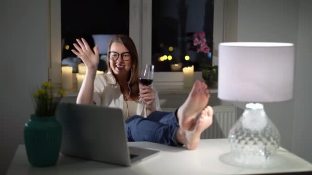 Jovem mulher trabalhando no computador portátil em casa à noite com vinho, chamada de vídeo — Vídeo de Stock