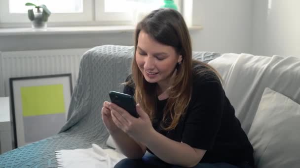 Jeune femme avec smartphone sur le canapé à la maison. Appareil de gadget téléphonique — Video