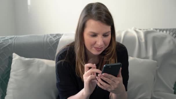 Evdeki kanepede akıllı telefonu olan genç bir kadın. Telefon aygıtı — Stok video