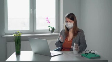 Salgın sırasında ofis maskesiyle dizüstü bilgisayarda çalışan genç bir kadın.