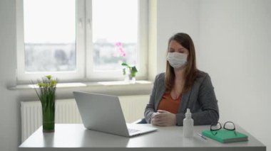 Salgın sırasında ofis maskesiyle dizüstü bilgisayarda çalışan genç bir kadın.