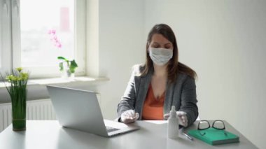 Salgın sırasında ofis maskesiyle dizüstü bilgisayarda çalışan genç bir kadın.
