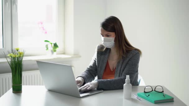 Молода жінка працює на портативному комп'ютері в офісній масці під час епідемії ковадла-19 — стокове відео