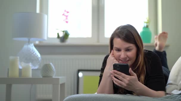 Jeune femme avec smartphone sur le canapé à la maison. Appareil de gadget téléphonique — Video