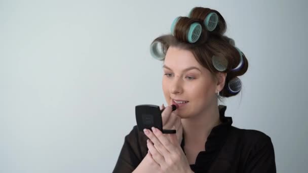 लिपस्टिक सह मेकअप करत केसांवर कर्लर रोलर्समध्ये तरुण स्त्री सुंदर मुलगी — स्टॉक व्हिडिओ