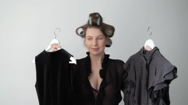 Junge Frau in Lockenwicklern auf Haaren und Dessous wählt Kleid aus dem Kleiderschrank — Stockvideo