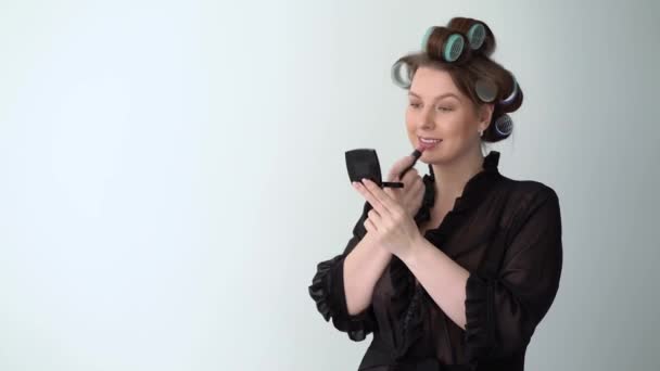 Ung kvinna i papiljotter rullar på hår gör makeup med läppstift vacker flicka — Stockvideo