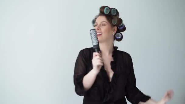 Woman with curlers rollers on hair and in bathrobe dancing singing in hairbrush. — Stock Video