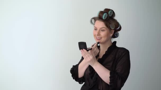Jovem mulher em rolos de rolos no cabelo fazendo maquiagem com batom Menina bonita — Vídeo de Stock