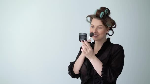 Mujer joven en rulos rodillos en el pelo haciendo maquillaje con cepillo, Hermosa chica — Vídeos de Stock