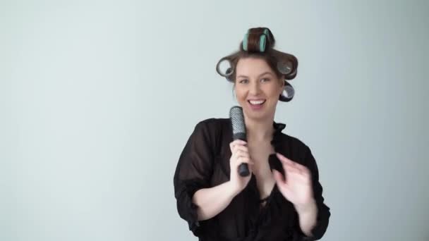 Женщина с бигуди роликами на волосах и в халате танцует пение в расческе . — стоковое видео
