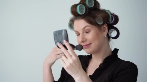Mujer joven en rulos rodillos en el pelo haciendo maquillaje con cepillo, Hermosa chica — Vídeos de Stock