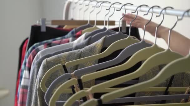 Mujer joven eligiendo ropa en un estante buscando qué ponerse. Tienda o armario — Vídeos de Stock