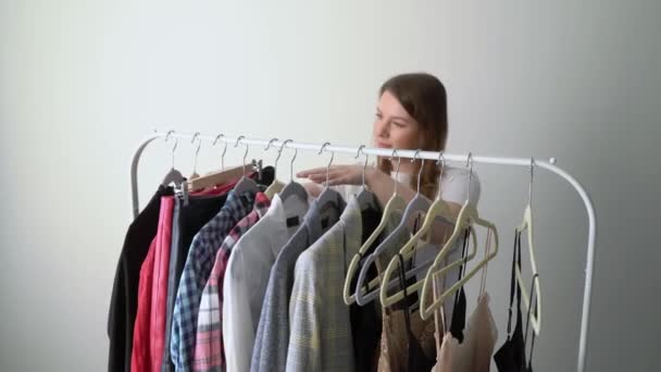 Mujer joven eligiendo ropa en un estante buscando qué ponerse. Tienda o armario — Vídeo de stock