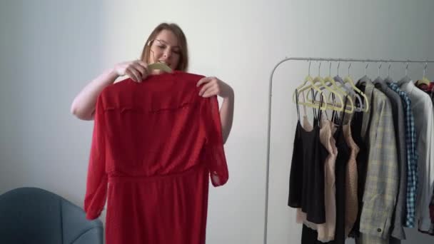 Ung kvinna väljer kläder på en rack söker vad man ska ha på sig. Förvaring eller garderob — Stockvideo