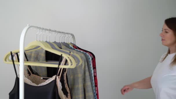 Giovane donna che sceglie i vestiti su un rack alla ricerca di cosa indossare. Negozio o armadio — Video Stock