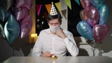 Genç adam doğum gününü yalnız kutluyor. Koruyucu tıbbi maskeli bir erkek.