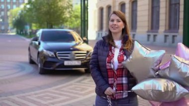Balon yıldızlı genç bir kadın, arkasında bir araba. Otomatik hediye ya da doğum gününde hediye
