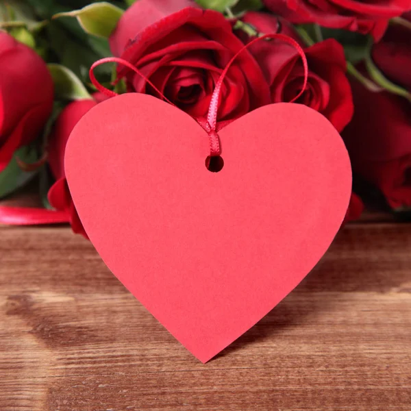 Valentinshintergrund aus Geschenkanhänger und roten Rosen auf Holz lizenzfreie Stockbilder