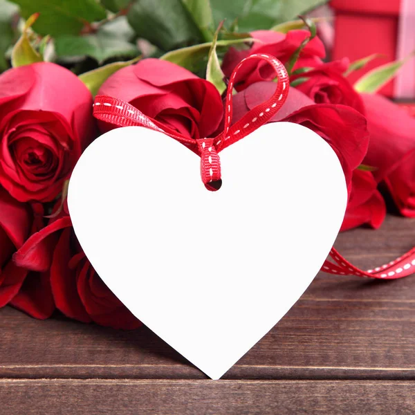 Valentinstag Hintergrund der weißen Geschenkanhänger und roten Rosen auf Holz. s lizenzfreie Stockfotos