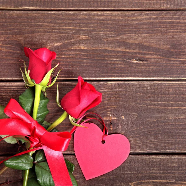 Valentinshintergrund aus Geschenkanhänger und roten Rosen auf Holz. Raum für lizenzfreie Stockfotos