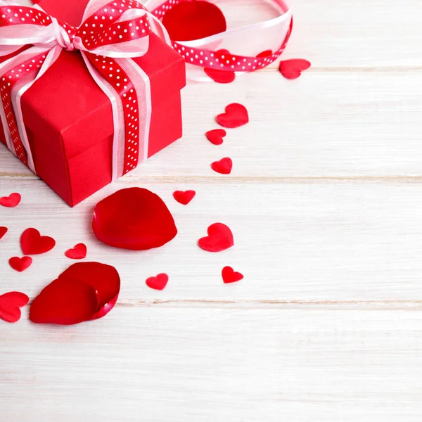 Valentinshintergrund der Geschenkbox und Rosenblätter auf weißem Holz. Stockfoto