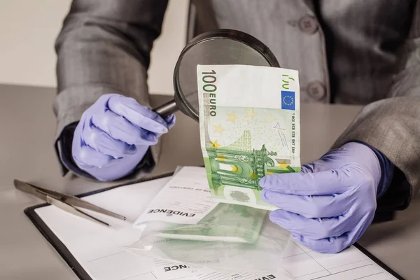 Policial com lupa verifica dinheiro suspeito — Fotografia de Stock