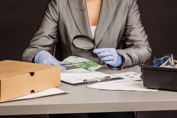 Mujer policía con lupa cheques dinero sospechoso —  Fotos de Stock