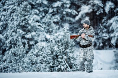 Kamuflaj, erkek avcısı silahlı bir tüfekle bir karlı kış ormanda ayakta