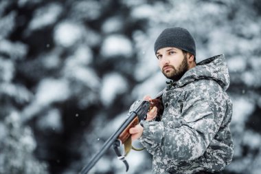 Kamuflaj, erkek avcısı silahlı bir tüfekle bir karlı kış ormanda ayakta