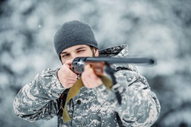 Kamuflaj, erkek avcısı silahlı bir tüfekle bir karlı kış ormanda ayakta