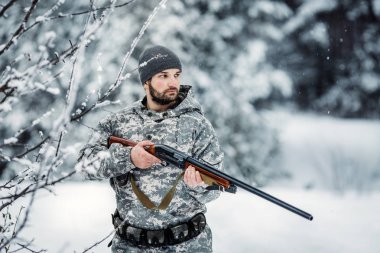 Kamuflaj, erkek avcısı silahlı bir tüfekle bir karlı kış ormanda ayakta