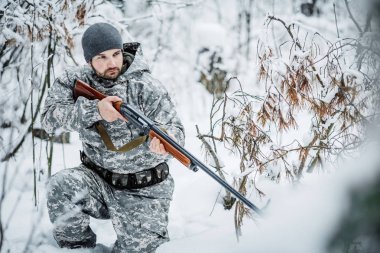 Kamuflaj, erkek avcısı silahlı bir tüfekle bir karlı kış ormanda ayakta
