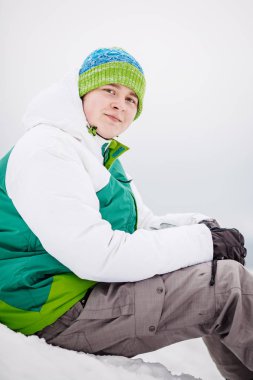 Snowboard ile kar üzerinde oturan genç adam