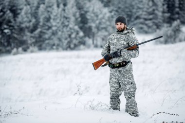 Kamuflaj, erkek avcısı silahlı bir tüfekle bir karlı kış ormanda ayakta