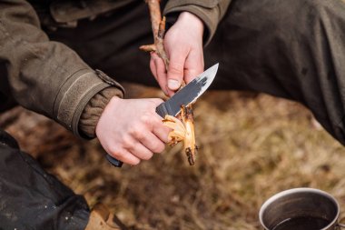 Yakın çekim el avcı bıçaklı adam ormanda kamp ateşi için tahta bir sopa kesti. Bushcraft, avcılık ve insan kavramı
