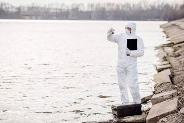Bilim adamı ya da bir tüp sıvı içeriğini inceleyerek koruyucu üniformaları giyen biyolog. Ekoloji ve çevre kirliliği kavramı.