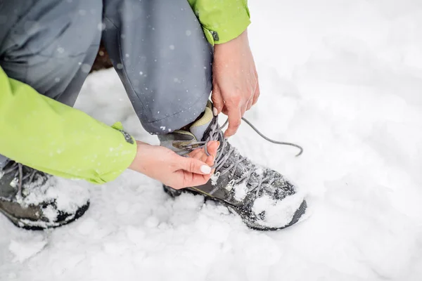 young woman hiker tying shoelace on winter forest