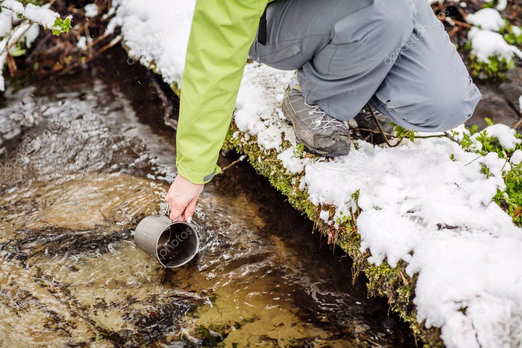 woman filling bottle of water from a winter forest stream. travel and vacation concept