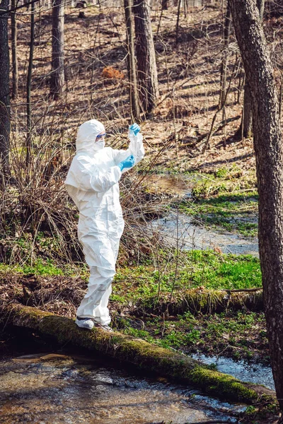 female scientist examining the liquid contents of a  test tube in the forest. Ecology and environmental pollution concept.