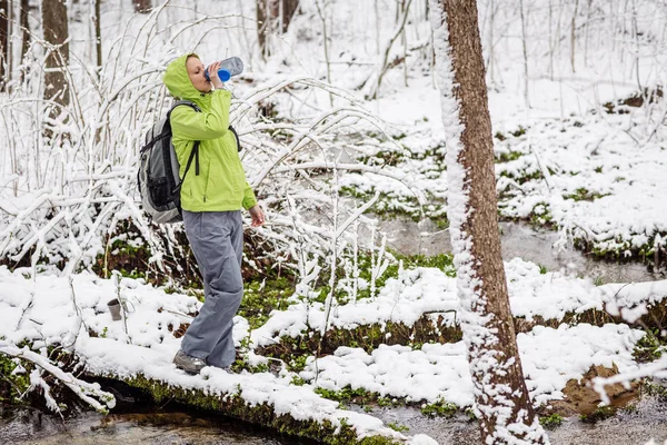 Woman filling bottle of water from a winter forest stream. — Stock Photo, Image