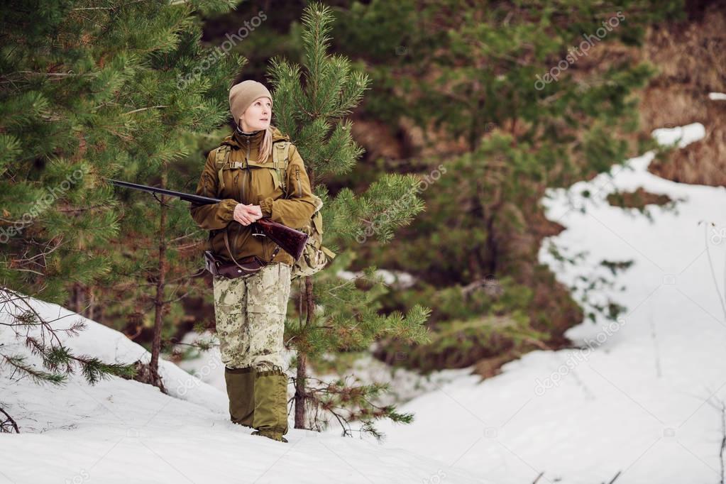 Female hunter in camouflage clothes ready to hunt, holding gun a