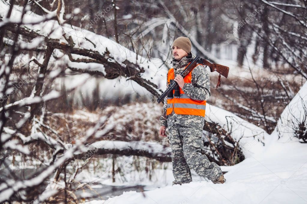 Male hunter in camouflage, armed with a rifle, standing in a sno