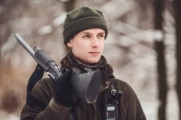 Manliga jägaren i kamouflage, beväpnad med ett gevär, stående i en sno — Stockfoto