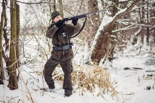 Manliga jägaren i kamouflage, beväpnad med ett gevär, stående i en sno — Stockfoto