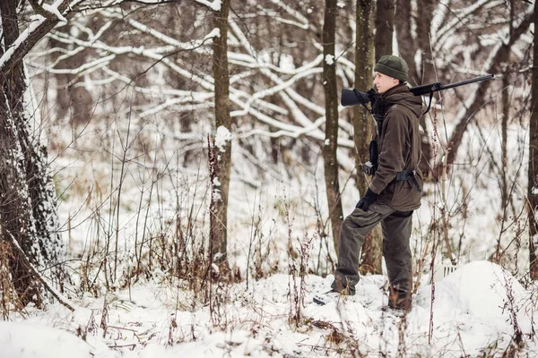 Manliga jägaren i kamouflage, beväpnad med ett gevär, stående i en sno — Stockfoto