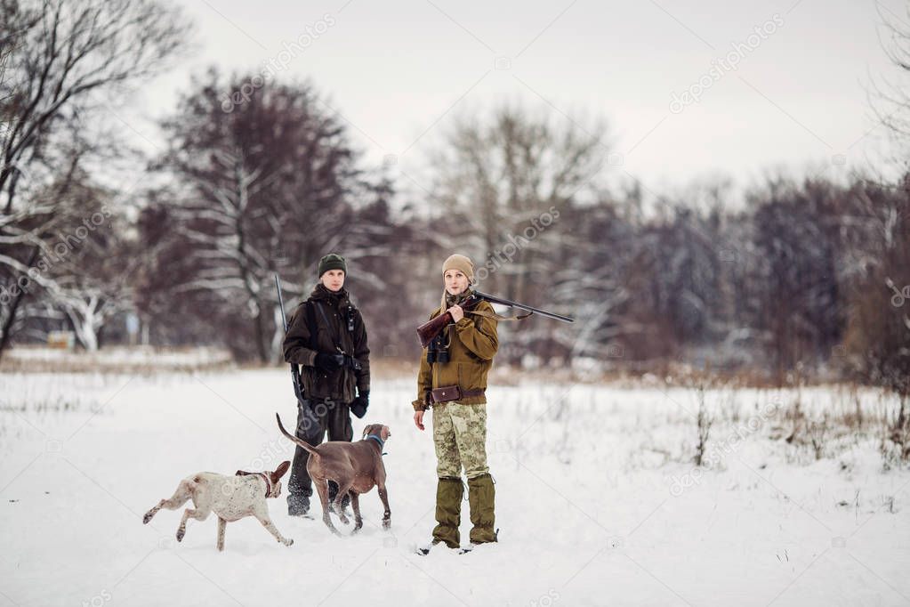 two hunters with rifles in a snowy winter forest. 