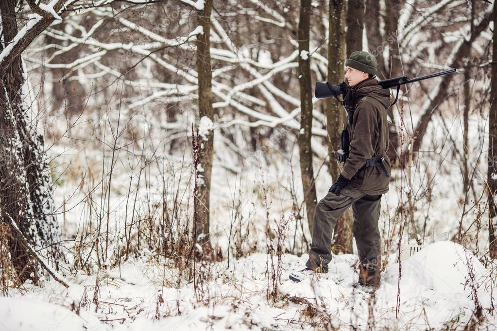 Male hunter in camouflage, armed with a rifle, standing in a sno