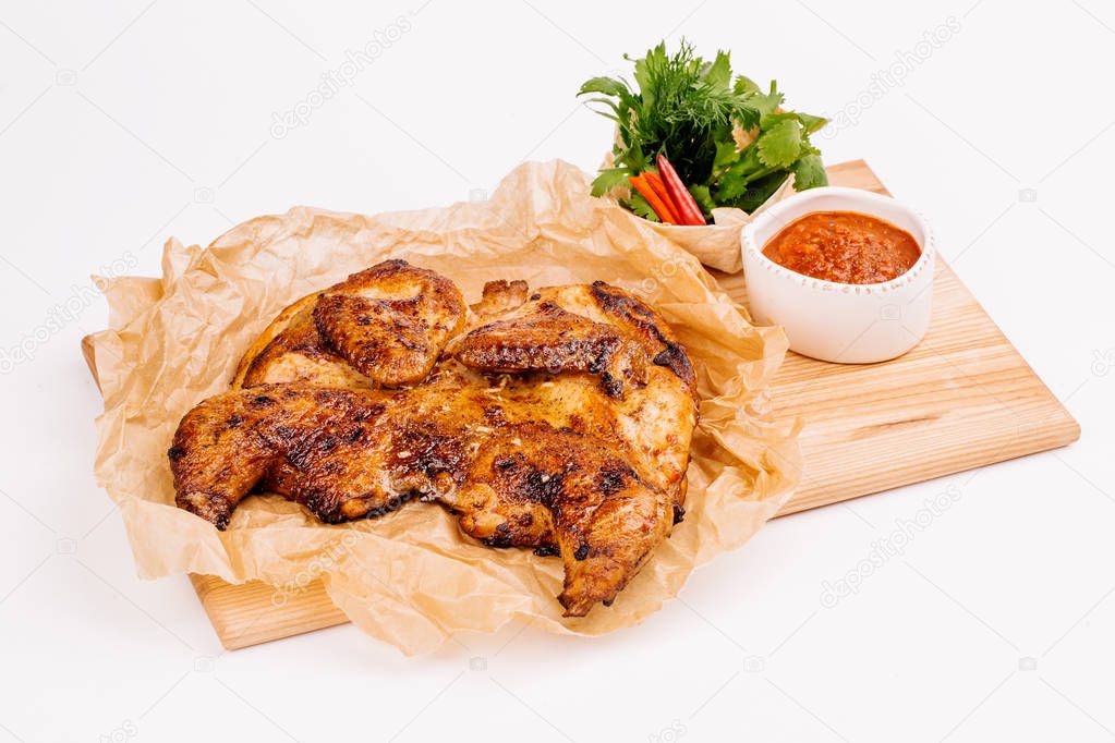 Grilled chicken Tabaka with sauce on a wooden plate on white bac